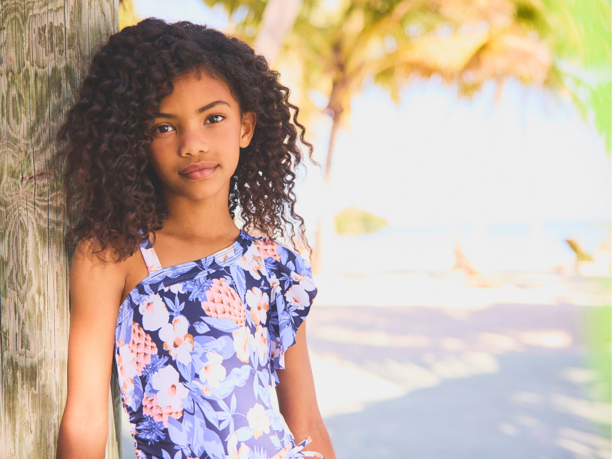 Young girl in floral dress leaning against palm tree at beach