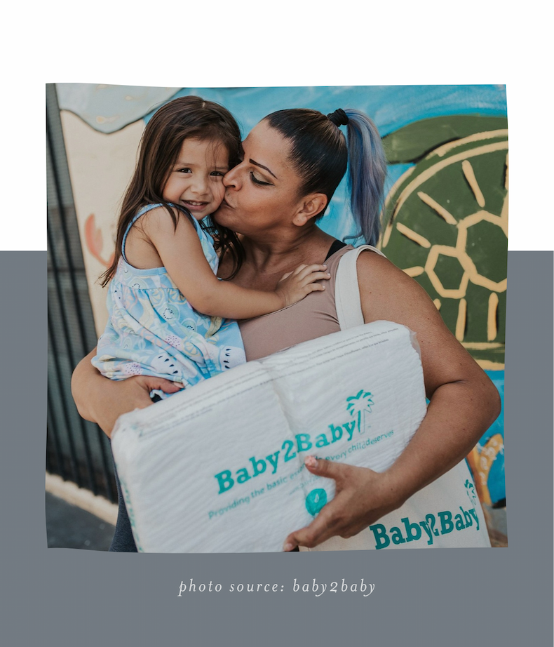 mom holding daughter and giving kiss on her cheek while holding pack of diapers