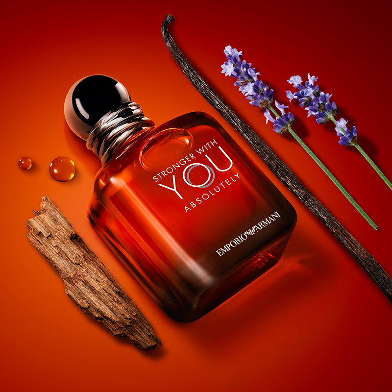 Armani Stronger With You Absolutely fragrance bottle surrounded by lavender and cedar wood on a warm amber backdrop.