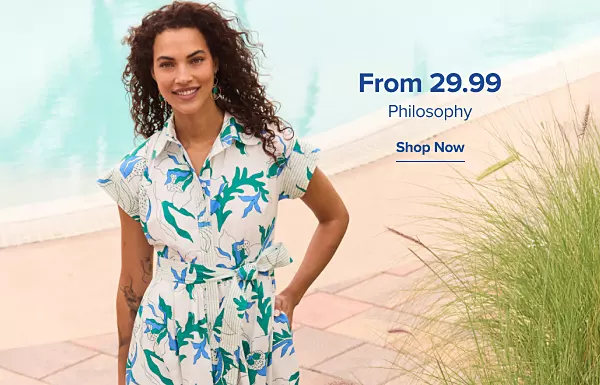 From 29.99 Philosophy. Shop now. A woman in a white, blue and green dress walking by a pool.
