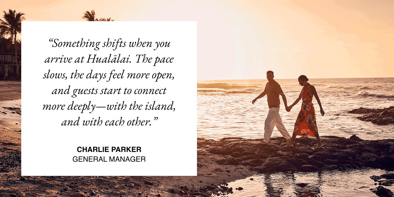 Couple walking hand in hand across black stones toward the beach. Text box overlay reads Something shifts when you arrive at Hualālai. The pace slows, the days feel more open, and guests start to connect more deeply—with the island, and with each other. Charlie Parker, General Manager.