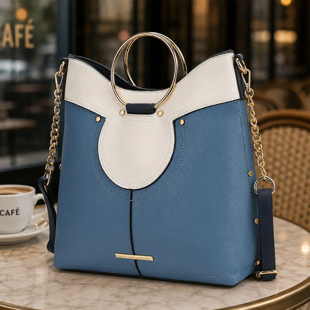 Blue and white colorblock handbag with gold ring handles displayed on café table
