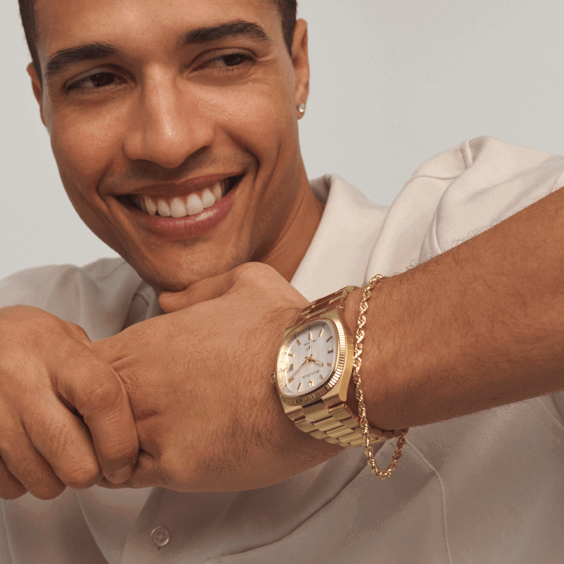 Man wearing gold watch with metal bracelet and gold chain bracelet.
