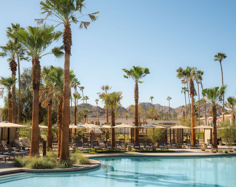 Resort pool at Kimpton Miralina Resort and Villas with palm trees, lounge chairs, and cabanas, set against mountains under a clear blue sky