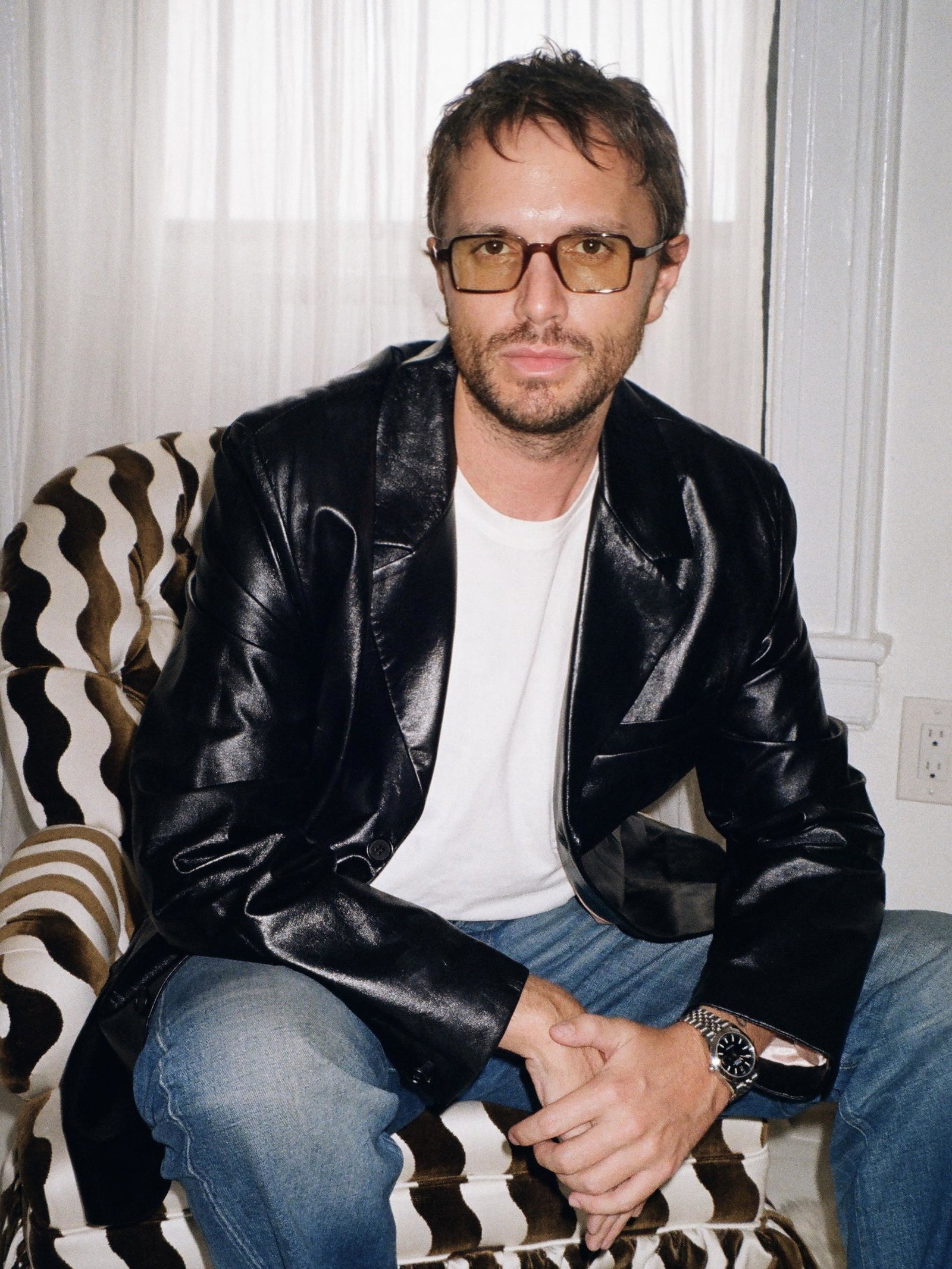 A person wearing a leather blazer and jeans sitting in a black and white striped chair.