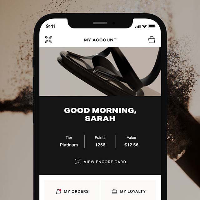 Smartphone screen displaying Brown Thomas Arnotts app with user account details, including tier status and points. Background shows coffee beans being ground.