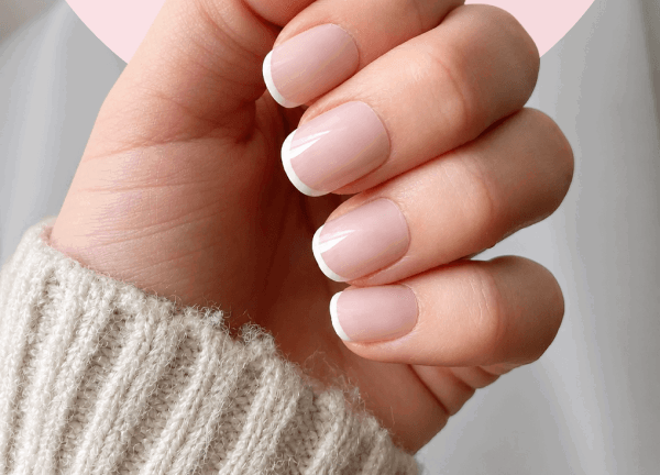 Light beige sweater sleeve showing manicured hand with short pale pink nude nail color