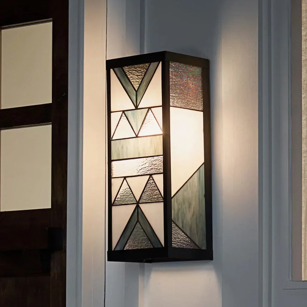 Modern black wall sconce with geometric glass panels and mixed textures mounted on white wall