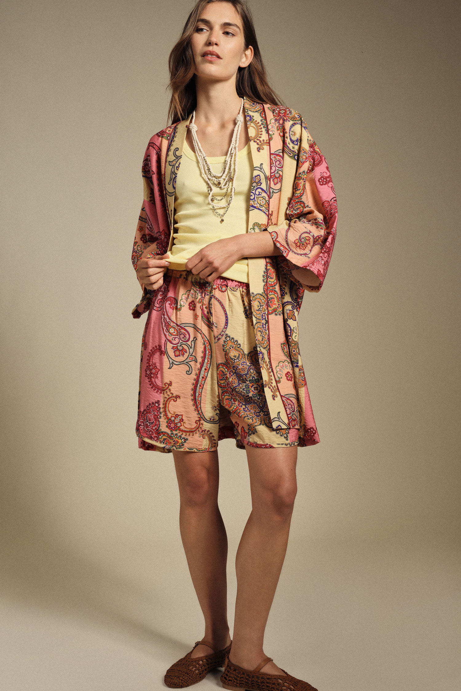 Woman in pink and yellow paisley kimono, matching shorts and yellow camisole with layered beaded necklaces