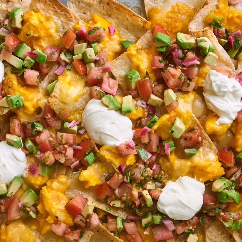 Tortilla chips with melted cheese, tomato, avocados, scrambled eggs, and dollops of sour cream.