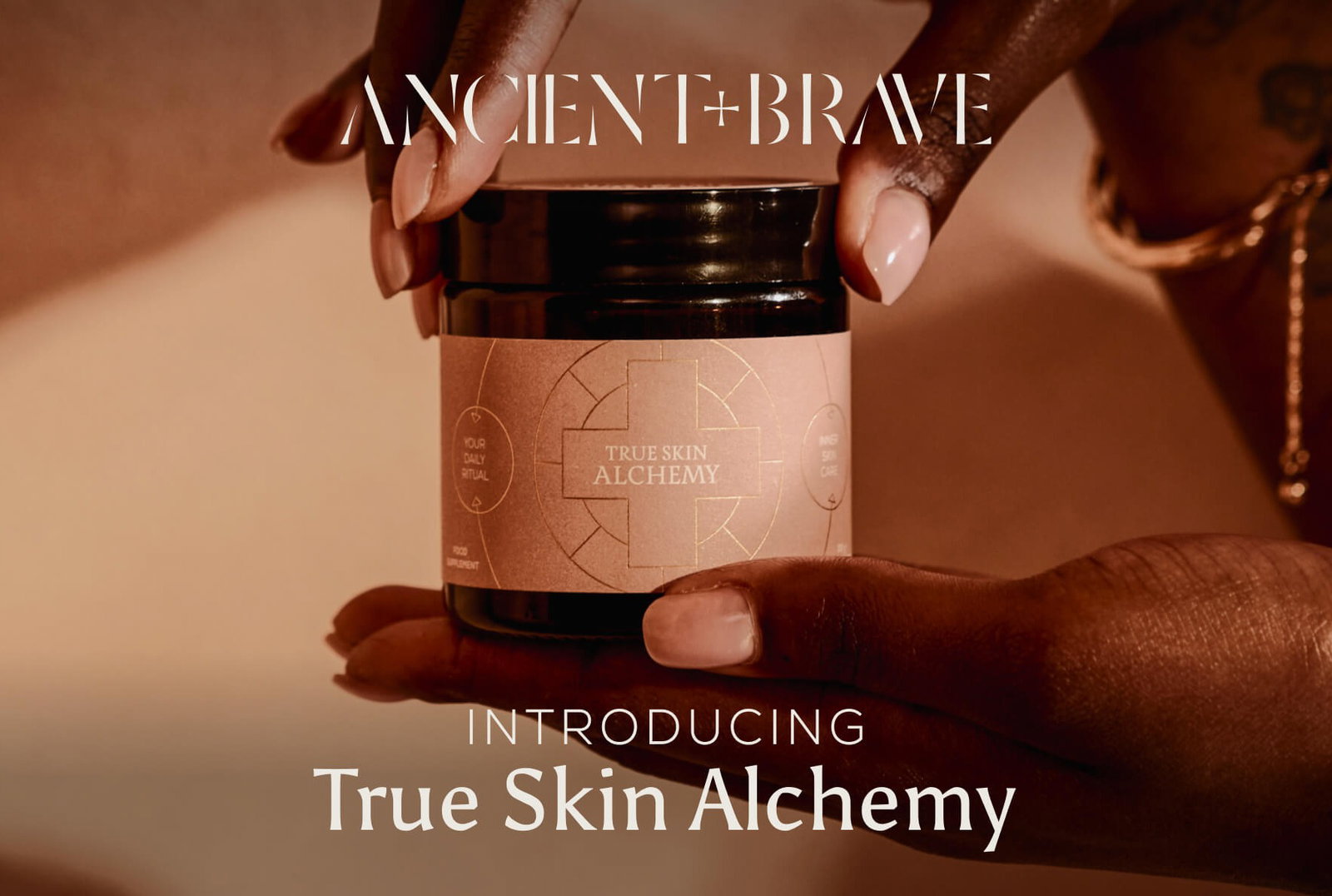 Ancient + Brave | Introducing True Skin Alchemy — hands cradling a dark glass jar of True Skin Alchemy supplement against a warm terracotta background