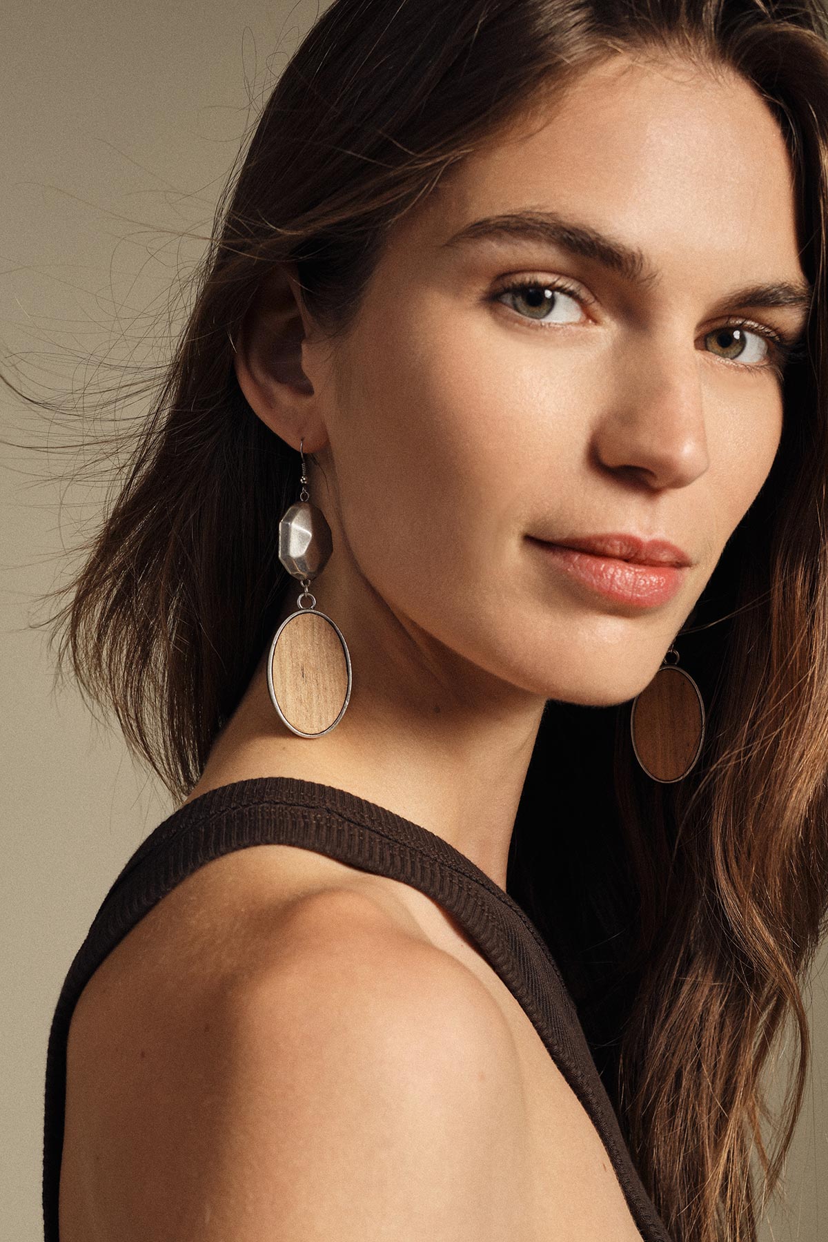 Close-up portrait of a woman wearing wooden oval drop earrings and a black tank top, neutral background and soft lighting