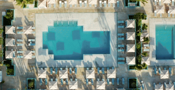 Hero Video GIF featuring 5 frames: 1) Bird's eye view of a pool. 2) Expansive view of property. 3) People splashing in the pool. 4) Two people ride their bike towards a historic monument by the sea. 5) Expansive view of shoreline. 