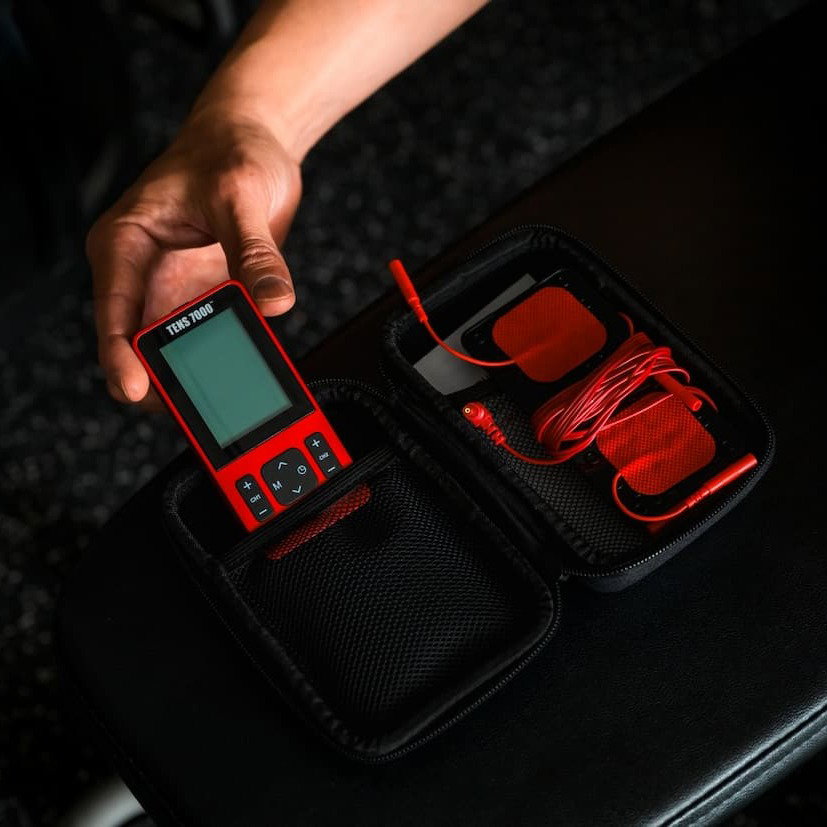 A hand pulling the TENS 7000 Sport Recovery TENS Unit from its case