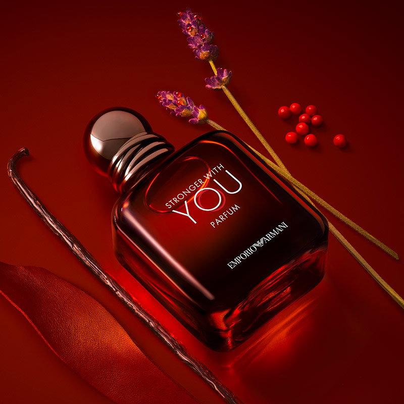 El frasco de la fragancia Armani Stronger With You Parfum expuesto sobre un fondo ámbar brillante con varitas de vainilla.