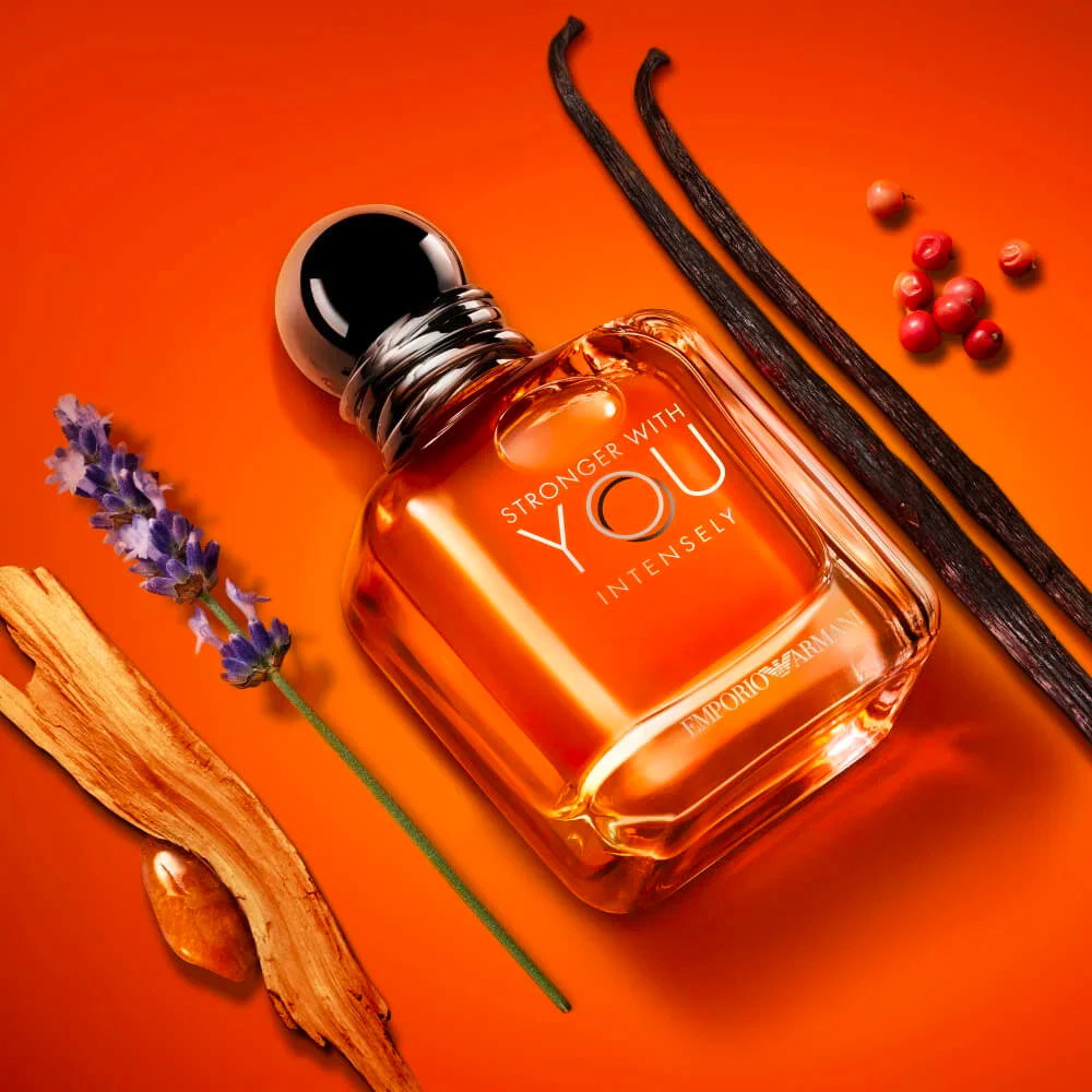 El frasco de la fragancia Armani Stronger With You Intensely rodeado de lavanda y varitas de ámbar sobre un fondo naranja brillante.