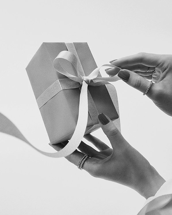 Ein Paar Hände mit manikürten Nägeln hält eine ordentlich verpackte Geschenkbox mit Schleife. Schwarz-weiß, vermittelt Eleganz und Vorfreude.
