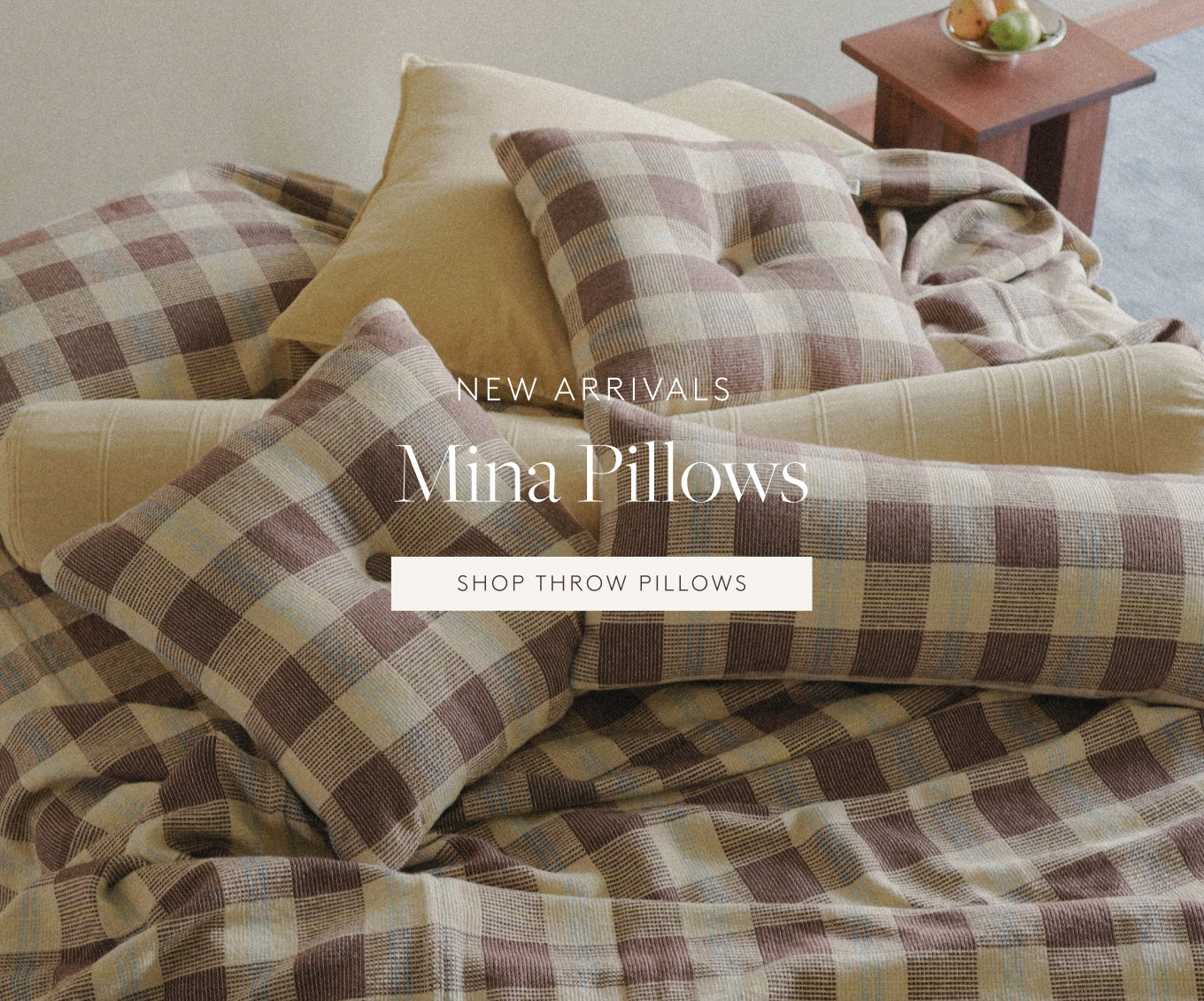 Stack of brown checked pillows on a bed next to a side table with fruit