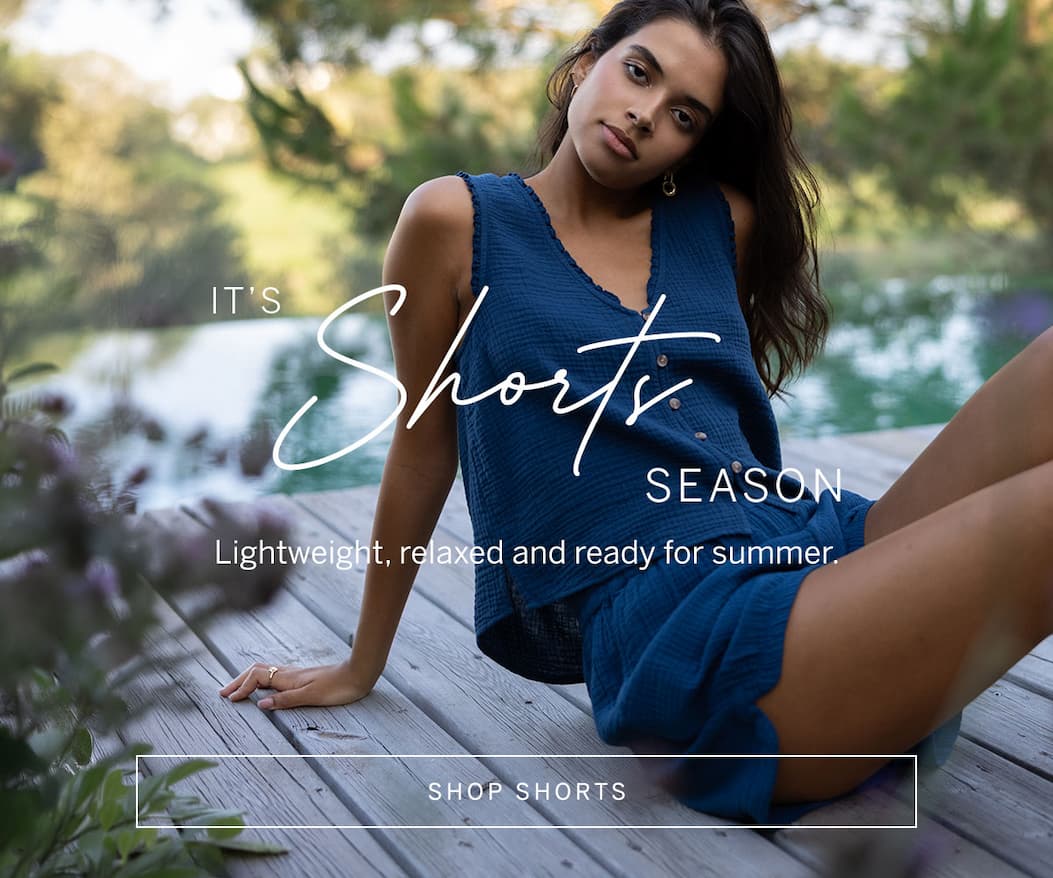 Model lounging beside a pool in a blue sleeveless top and matching shorts. Text reads: “It’s Shorts Season. Lightweight, relaxed and ready for summer.”