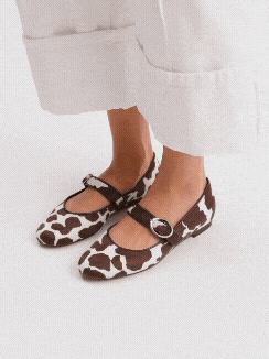Woman wearing cow print Mary Jane flats with white trousers, multiple angles