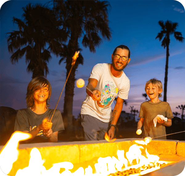 A father and his two children roast marshmallows over a campfire.