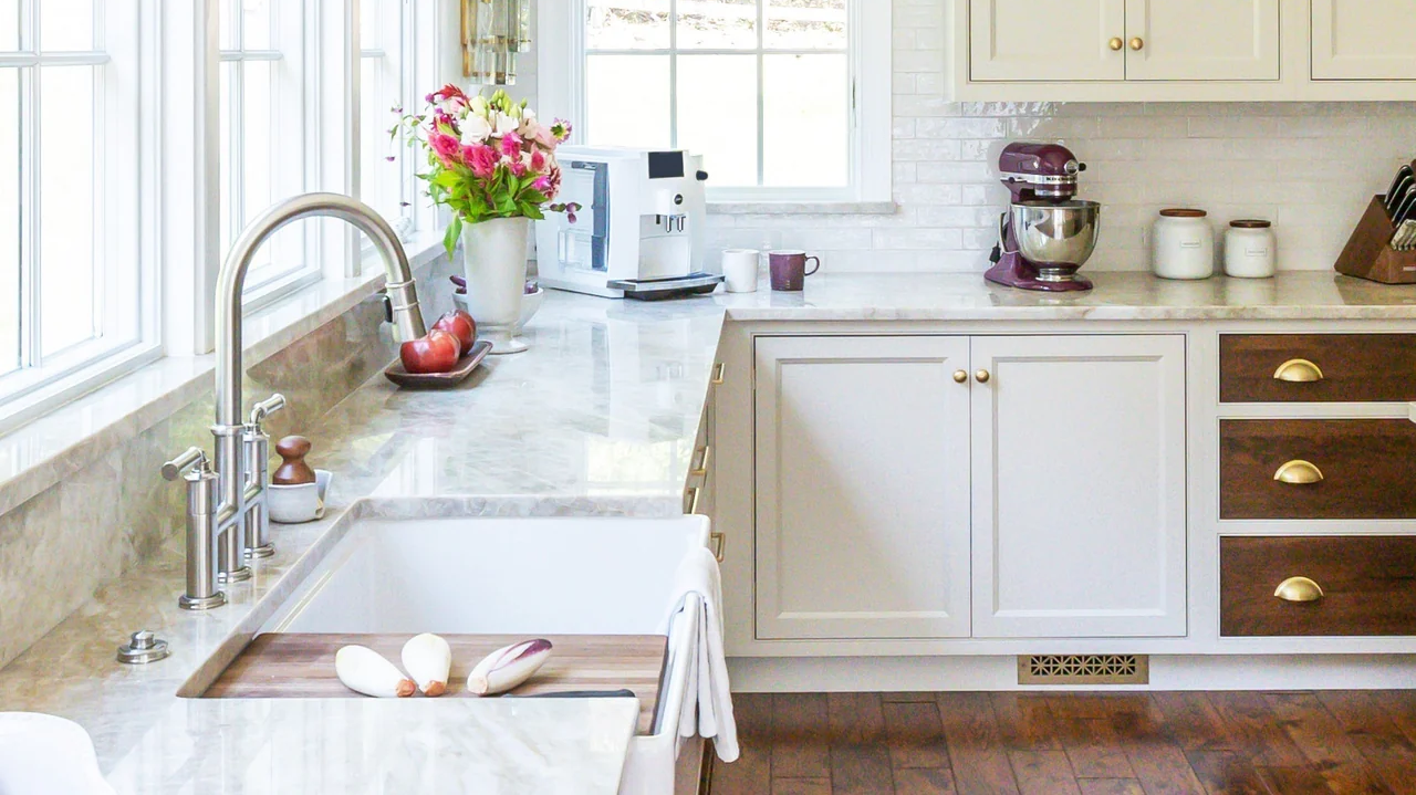 Designer Kelly Manas's sunny kitchen in tones of white with brass accents sports a Reggio Registers Toe Kick Asher Pattern vent in Sun Gold.