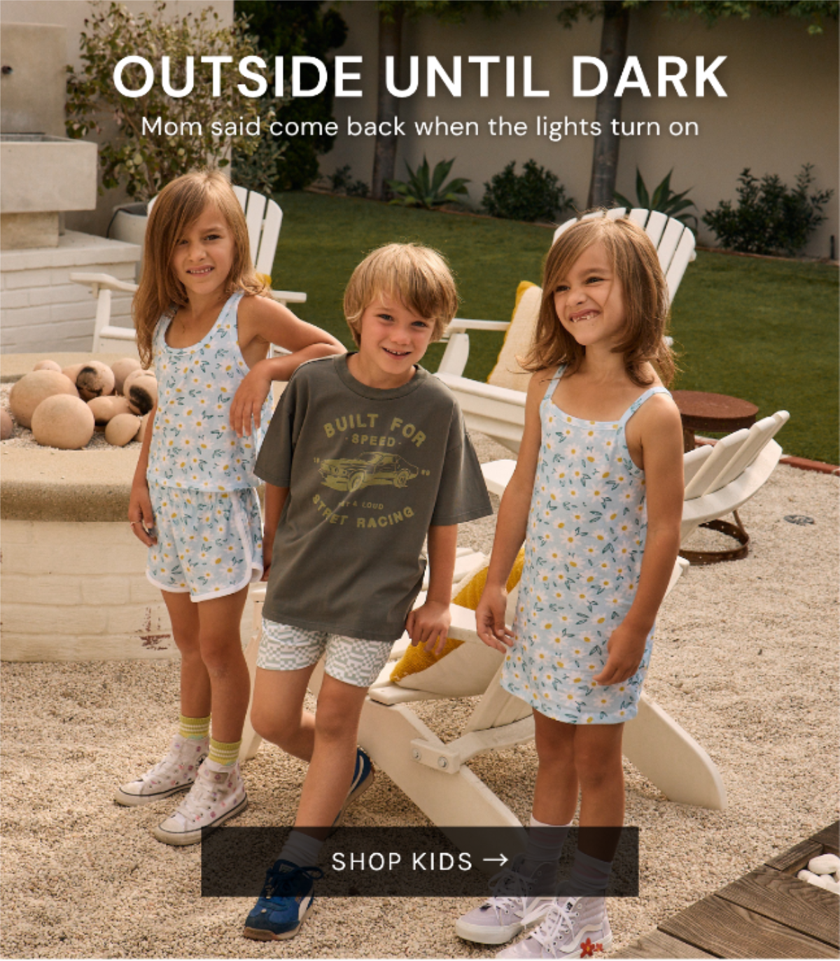 Chaser Kids Summer 2026 collection featuring two girls in matching floral dresses and a boy in a vintage-inspired graphic tee gathered outdoors in a sunny backyard setting