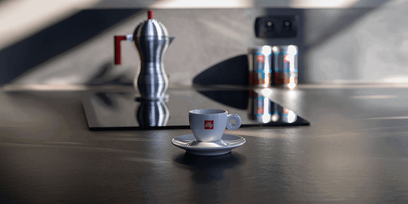 Illy espresso cup on a countertop with a moka pot and coffee tins in the background