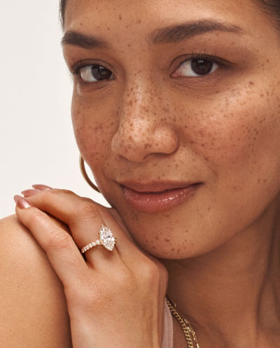 Female model wearing marquise-cut diamond engagement ring with yellow gold band and hoop earrings.