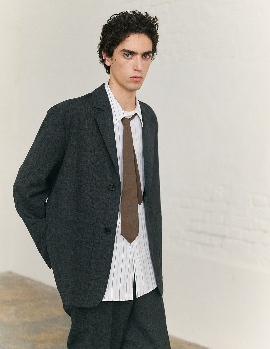 Dark relaxed blazer layered over a white shirt and brown tie