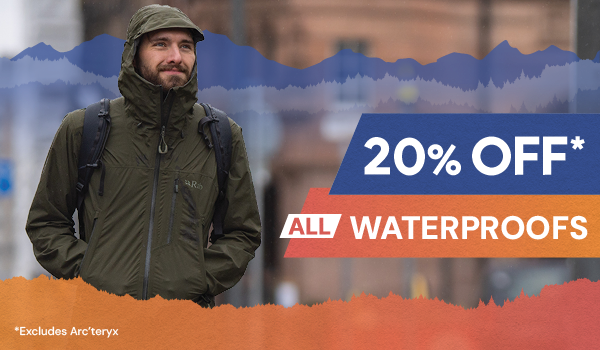 20% OFF ALL WATERPROOFS* *Excludes Arc'teryx. A man walks through a city in the rain wearing Rab Men's Downpour Mountain Jacket in Green. 