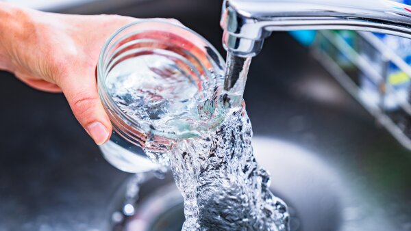 A close-up image of water pouring from a faucet and overflowing in a clear glass above the sink.