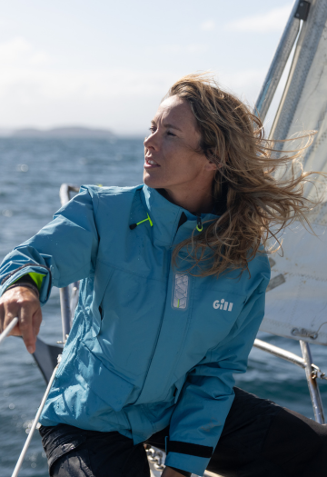 Woman sat at the bow of a boat with blue sailing jacket