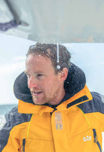 Man in gold/yellow sailing jacket with water spray from rough sea
