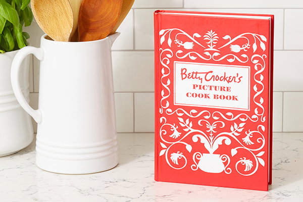 Betty Crocker's Picture Cook Book on a kitchen counter with jar of spoons