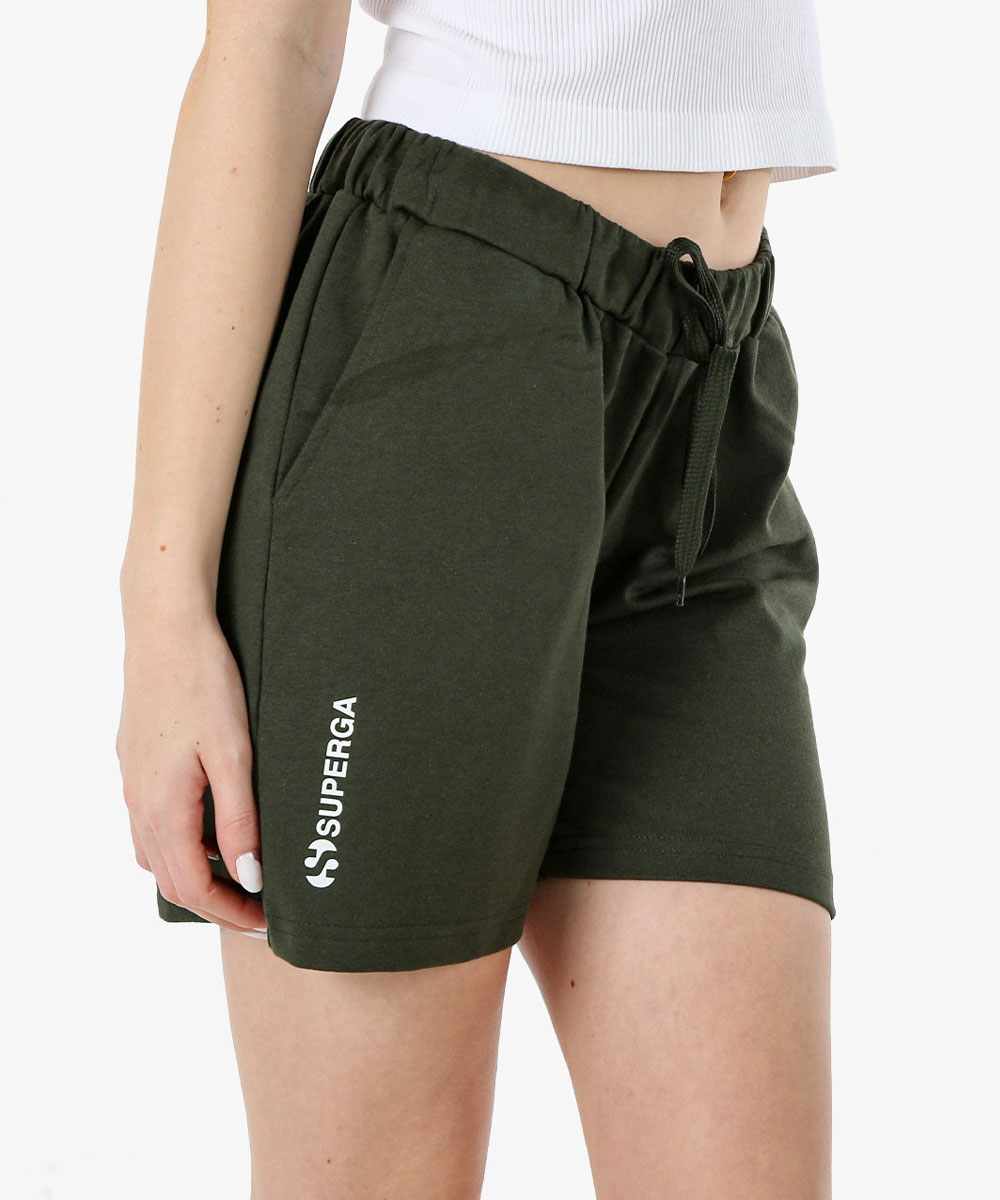 Close-up of woman wearing dark green Superga drawstring shorts with white logo and a white cropped top, hand resting by her thigh
