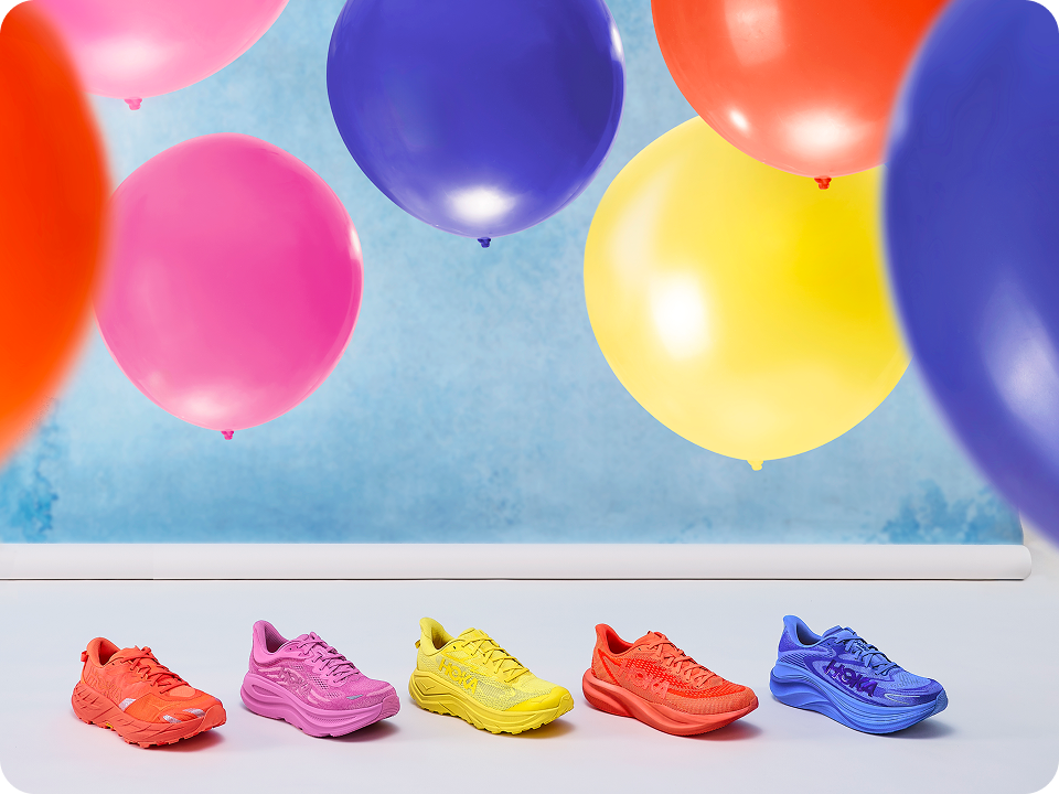Image of a group of colorful shoes resting on a gray floor with a blue background and colorful balloons floating in the air.