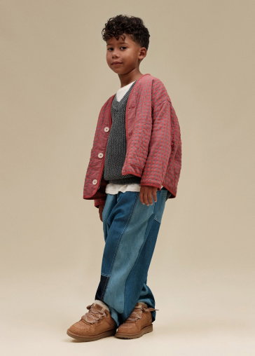 A studio shot of a model posing with a leg in the air, wearing a hat, t-shirt, trousers and kids' GoldenGlow Sandals