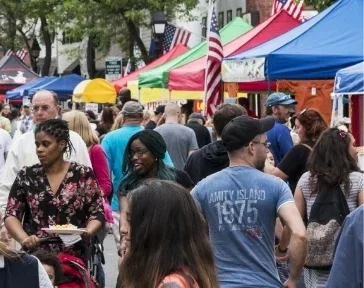 People, tents and flags crowd an outdoor market on a bright summer day.