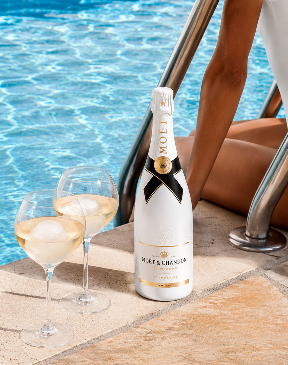Moët & Chandon Ice Impérial bottle by pool ladder with two chilled wine glasses containing ice and tanned swimmer's legs