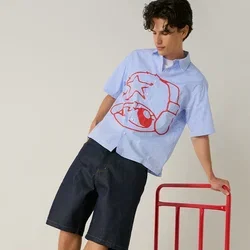 Jeune homme en équilibre sur un chariot plateforme rouge, portant un t-shirt bleu avec un motif rouge, un short noir, des chaussettes blanches et des baskets rouges, sur fond uni.