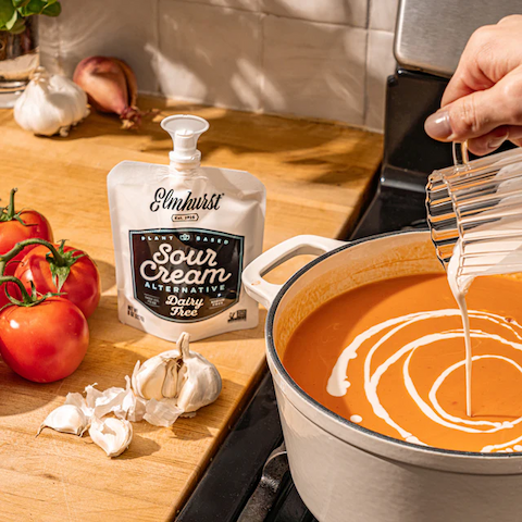 Dairy free sour cream on a kitchen counter beside a pot of warm tomato soup. 