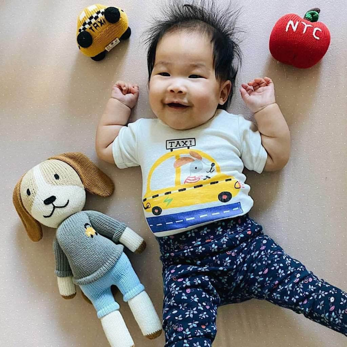 Baby wearing NYC taxi onesie surrounded by organic knit toys from the Little Explorers NYC Set