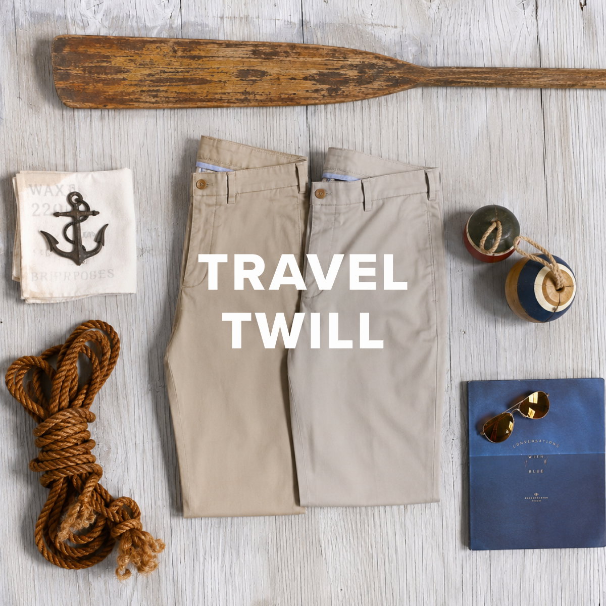 Two pairs of Bills Khakis Travel Twill pants sit folded alongside vintage maritime items