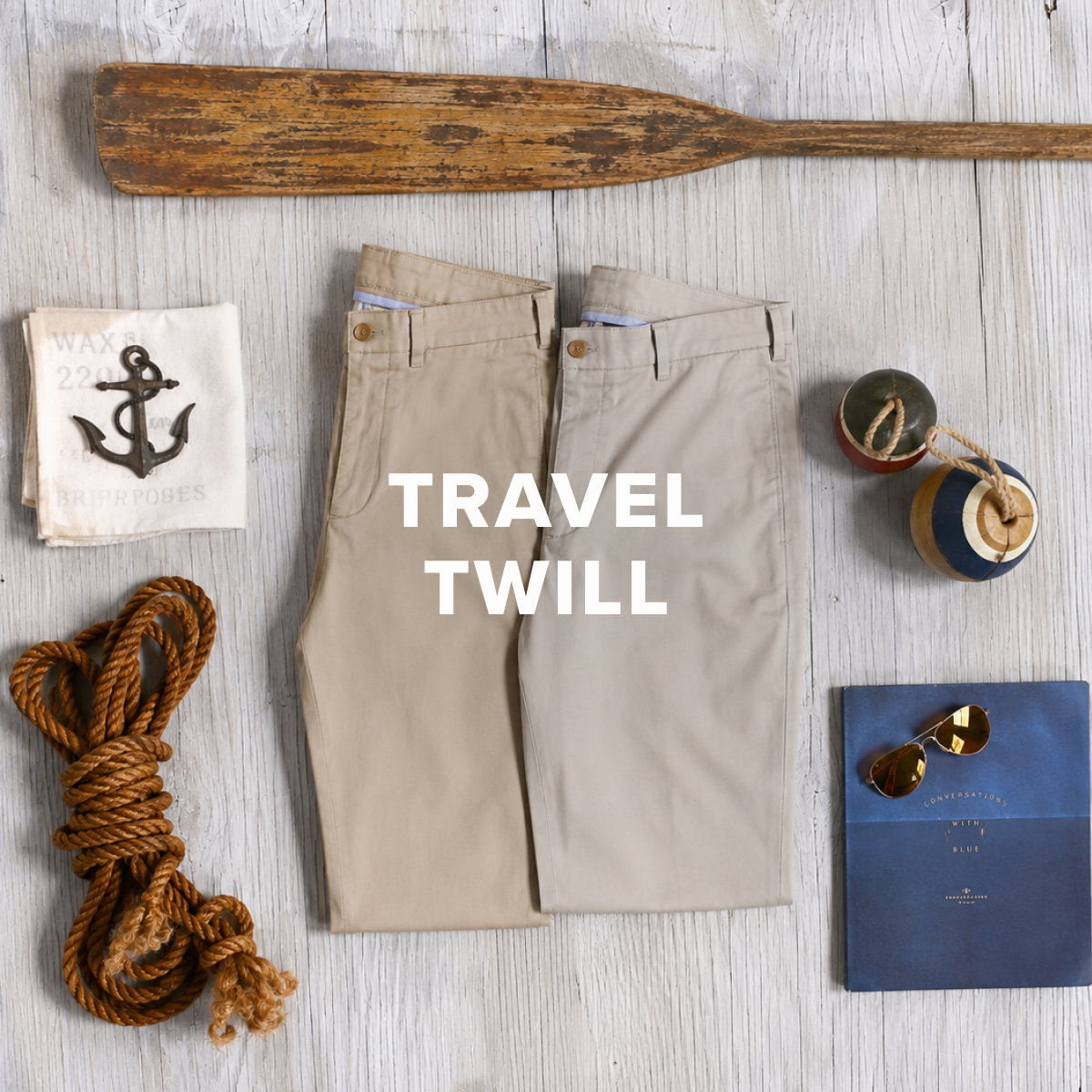 Two pairs of Bills Khakis Travel Twill pants sit folded alongside vintage maritime items
