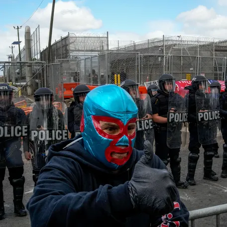 A person wearing a lucha libre mask gives a thumbs up next to Newark police officers in riot gear outside the Delaney Hall detention center in Newark, New Jersey, U.S., May 30, 2026.