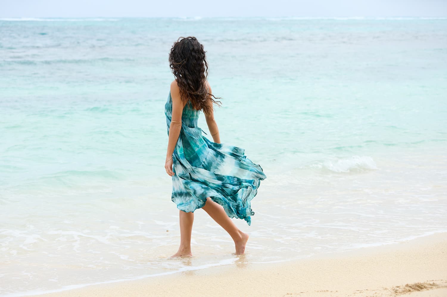 Woman wearing teal tie-dye dress walking on the beach