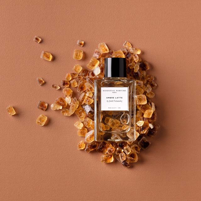 Perfume bottle labeled 'Amber Latte' surrounded by amber-colored crystals on a light brown background.