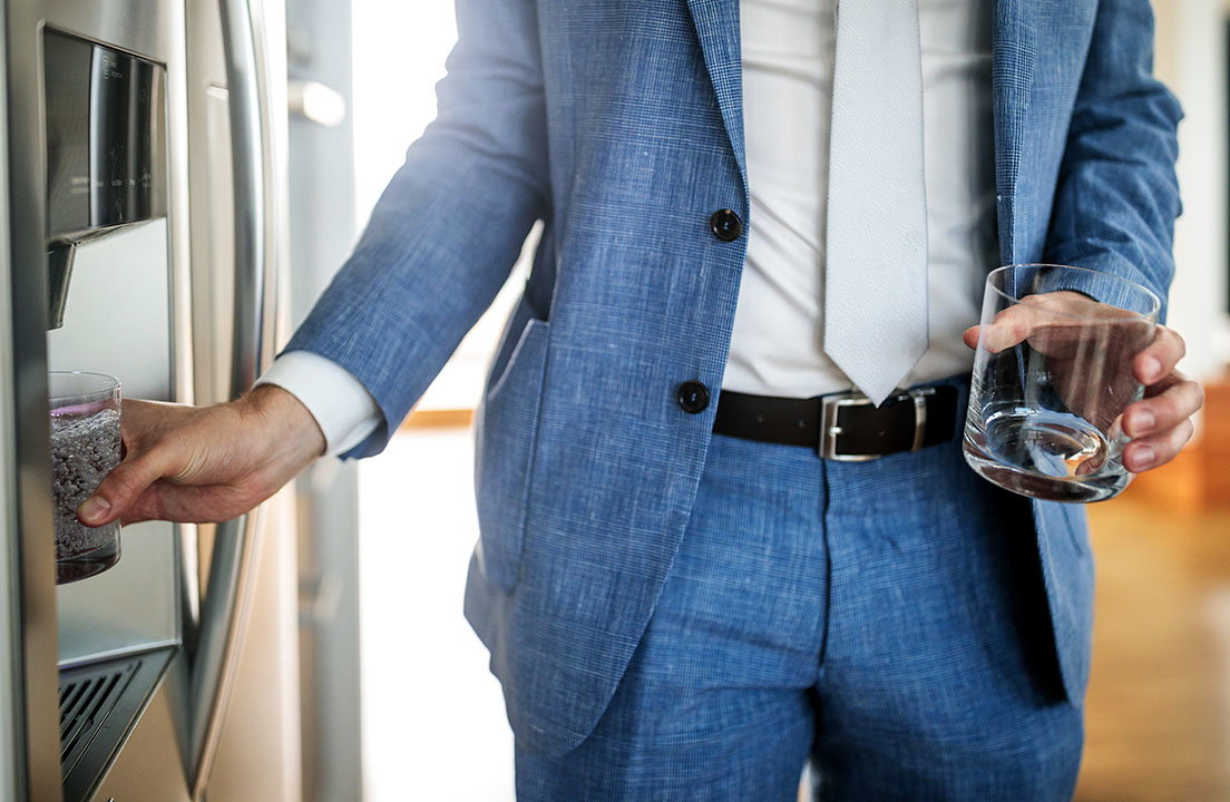A man fills a glass with water from a refrigerator dispenser while holding an empty glass