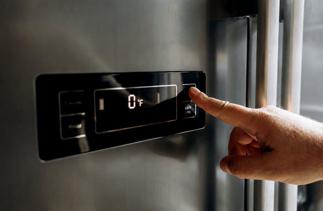 A hand adjusts a refrigerator control panel showing the freezer temperature set to 0°F
